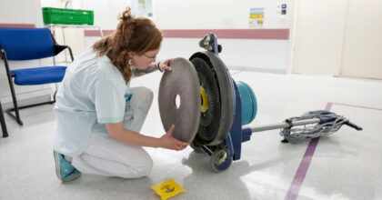 Eine Frau kniet am Boden und wechselt an einer Reinigungsmaschine das Reinigungspad aus.