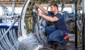 Ein Mann kniet in einem Flugzeug-Cockpit und verlegt diverse Kabel.