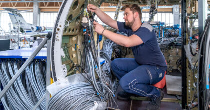 Ein Mann kniet in einem Flugzeug-Cockpit und verlegt diverse Kabel.