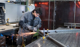 Eine Frau mit Schutzbrille steht an einem Tisch und flext an einem Metallrahmen.