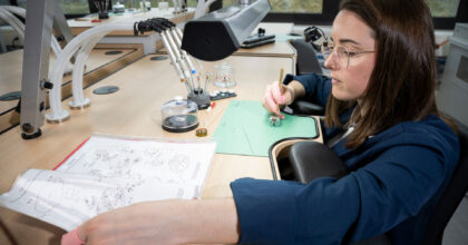 Eine Frau montiert nach einem Plan ein Uhrwerk.