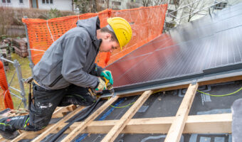 Ein Mann montiert auf dem Dach eines Hauses Solarpanels.