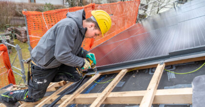 Ein Mann montiert auf dem Dach eines Hauses Solarpanels.