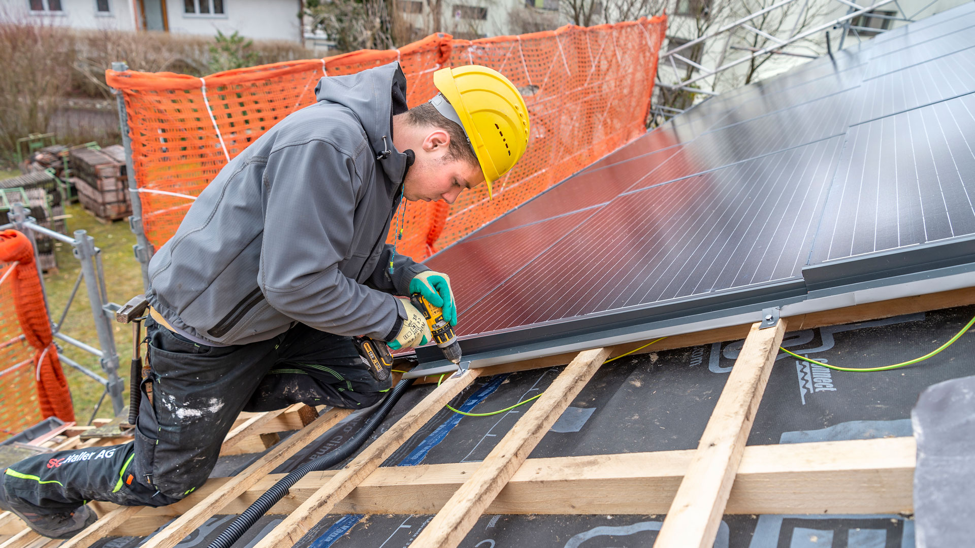 Ein Mann montiert auf dem Dach eines Hauses Solarpanels.