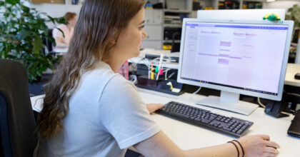 Eine Frau sitzt vor dem Computerbildschirm und führt mit der rechten Hand die Computermaus.
