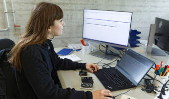 Eine Frau sitzt an einem Tisch mit einem Laptop vor sich und schaut auf den externen Bildschirm.