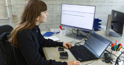 Eine Frau sitzt an einem Tisch mit einem Laptop vor sich und schaut auf den externen Bildschirm.