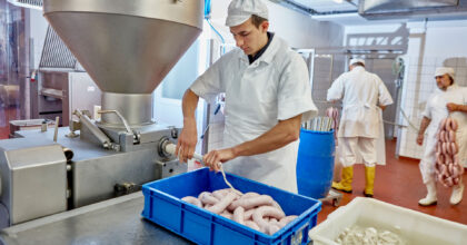 In einer Metzgerei füllt ein Mann Würste in eine Wursthülle.