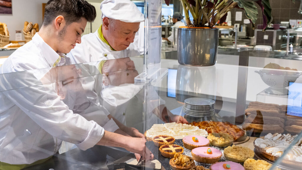 Zwei Männer drapieren süsse Köstlichkeiten in einer Vitrine.