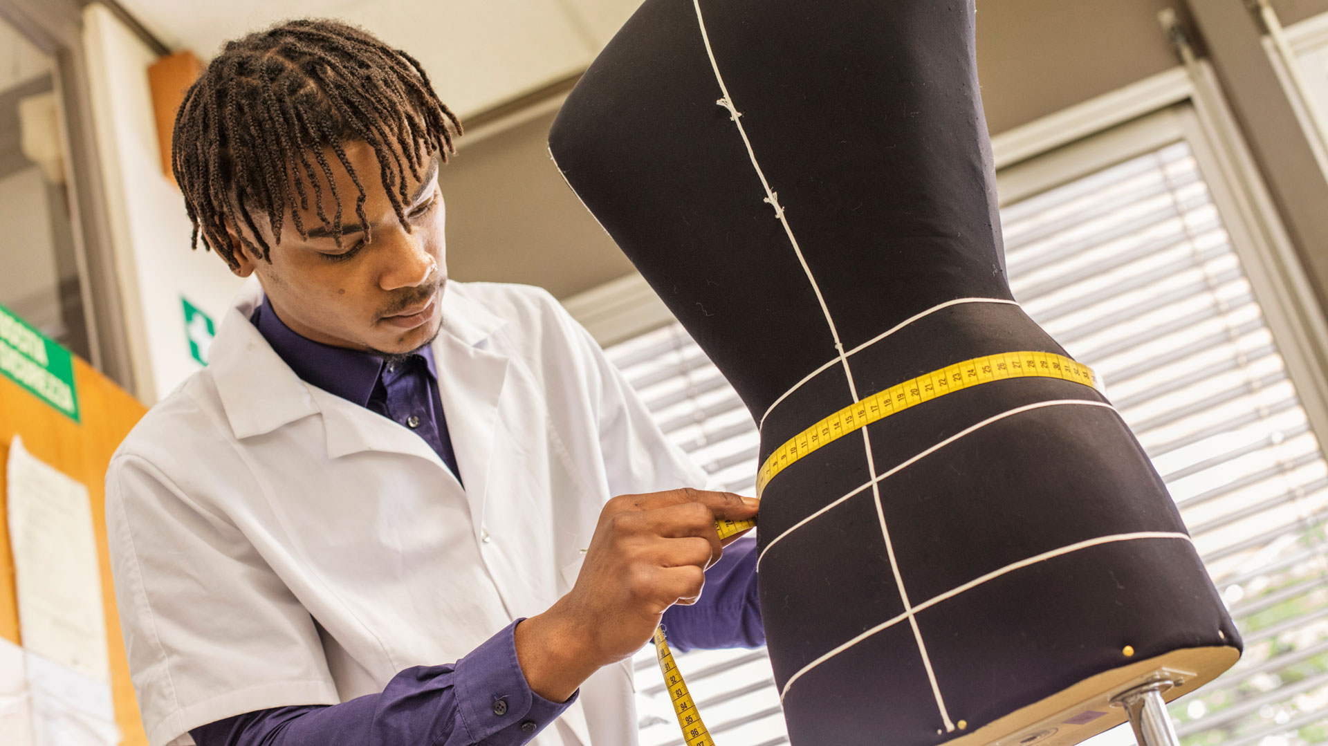 Ein Mann misst mit einem Centimetermass an einer Schneiderpuppe den Taillenumfang.