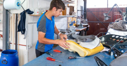 Ein Mann entfernt an einem ausgebauten Autositz den alten Bezug.