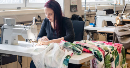 Eine Frau sitzt an einer Nähmaschine und näht an einem bunten Nachtvorhang.