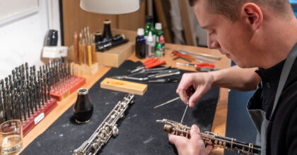 Ein Mann justiert mit einem Werkzeug die Tasten einer Klarinette.