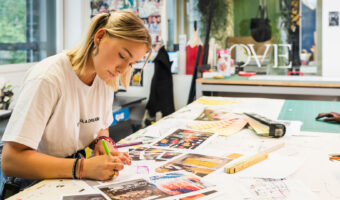 Eine junge Frau sitzt an einem Arbeitstisch und skizziert ein neues Projekt.