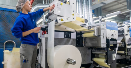 Eine Frau steht an einer Maschine und richtet zu bedruckendes Material für eine Verpackung ein.