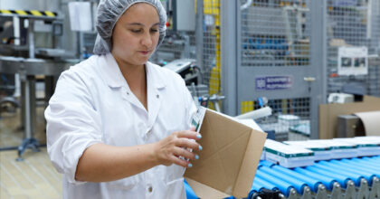 Eine Frau steht an einem Fliessband und prüft eine Kartonschachtel.