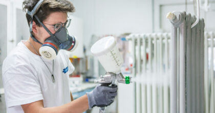 Ein Mann mit Schutzmaske lackiert mit einer Spritzpistole einen Radiator.