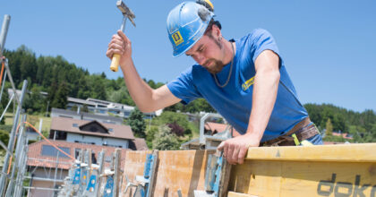 Ein Mann befestigt auf einem Gebäude eine Wandschalung aus Holz.