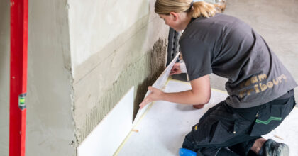 Eine Frau kniet am Boden und befestigt eine Keramikplatte an der Wand.
