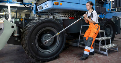 Eine Frau löst an einem Bagger die Radmutter mit einem langen Werkzeug.