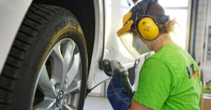 Eine Frau mit Schutzmaske schleift die eingedrückte Tür eines Autos.