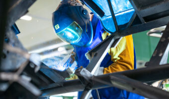 Ein Mann mit Schutzmaske schweisst an einem Autorahmen.