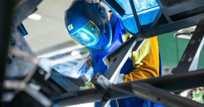 Ein Mann mit Schutzmaske schweisst an einem Autorahmen.