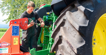 Ein junger Mann hantiert an der Anhänger-Kupplung eines Traktors.