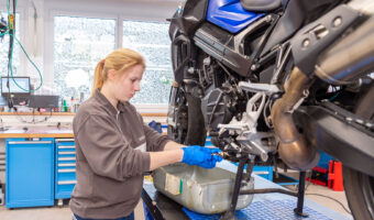 Eine junge Frau macht in der Werkstatt einen Ölwechsel an einem grossen Motorrad.