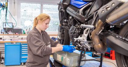 Eine junge Frau macht in der Werkstatt einen Ölwechsel an einem grossen Motorrad.