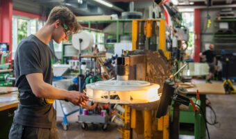 Ein junger Mann mit Schutzbrille hantiert an einem grossen Teil aus Kunststoff.
