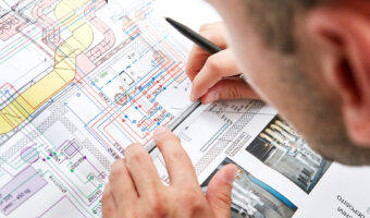 Ein Mann sitz über einem Plan und zeichnet weitere Details ein.