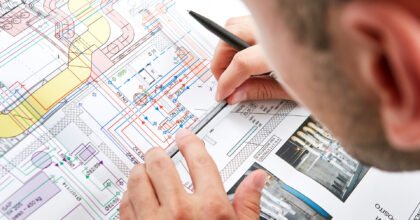 Ein Mann sitz über einem Plan und zeichnet weitere Details ein.