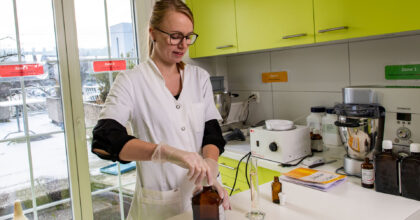 Eine Frau in weissem Arbeitskittel mixt eine Tinktur zusammen.