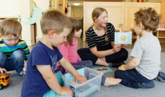 Eine Frau sitzt mit vier kleinen Kindern am Boden und erzählt eine Geschichte.